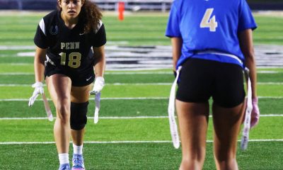 Two women on a football field, one in a black uniform and the other in a blue uniform, both wearing cleats