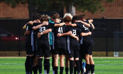 A group of soccer players, all wearing black uniforms, huddle together on a field, celebrating their victory