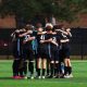 A group of soccer players, all wearing black uniforms, huddle together on a field, celebrating their victory