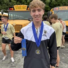 Evan Wilson after New Prairie Invite holding a first place ribbon and wearing a medal.