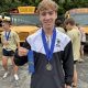Evan Wilson after New Prairie Invite holding a first place ribbon and wearing a medal.