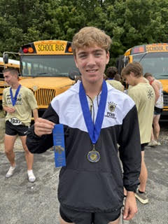 Evan Wilson after New Prairie Invite holding a first place ribbon and wearing a medal.