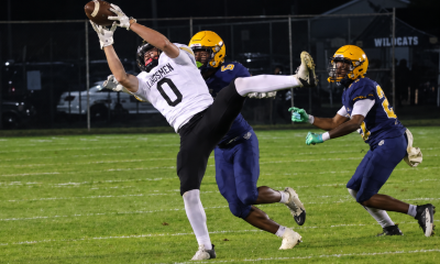 Football player in motion, reaching for the ball, with the goalie and other players in the background.