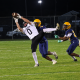 Football player in motion, reaching for the ball, with the goalie and other players in the background.