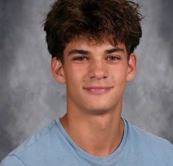 A young man with a short hairstyle, wearing a blue shirt, poses for a school portrait.