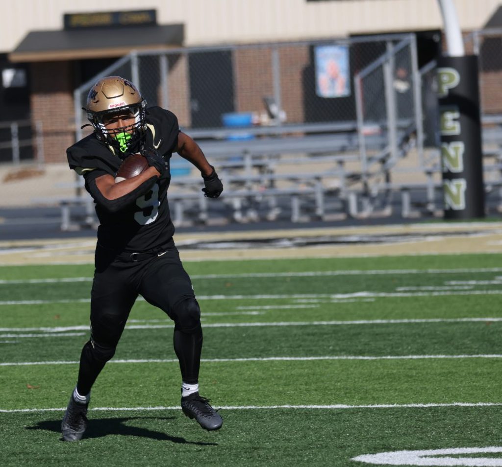 A football player runs on the field carrying a football.