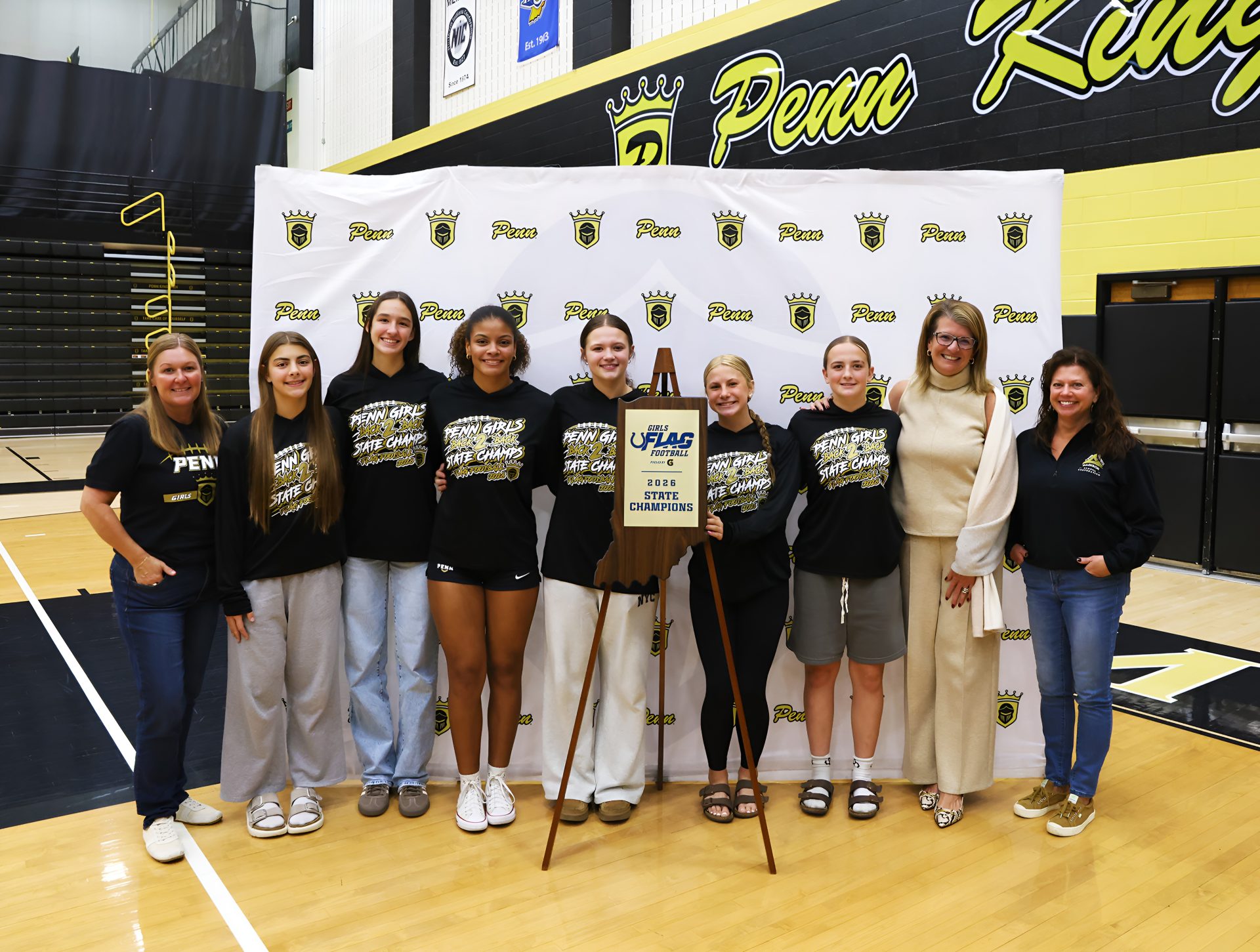 A group of young athletes posing for a photo with a trophy, a woman, and a man in a suit