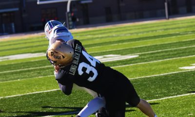 Football player in black uniform with number 34, in mid-air, reaching for a ball, with a white