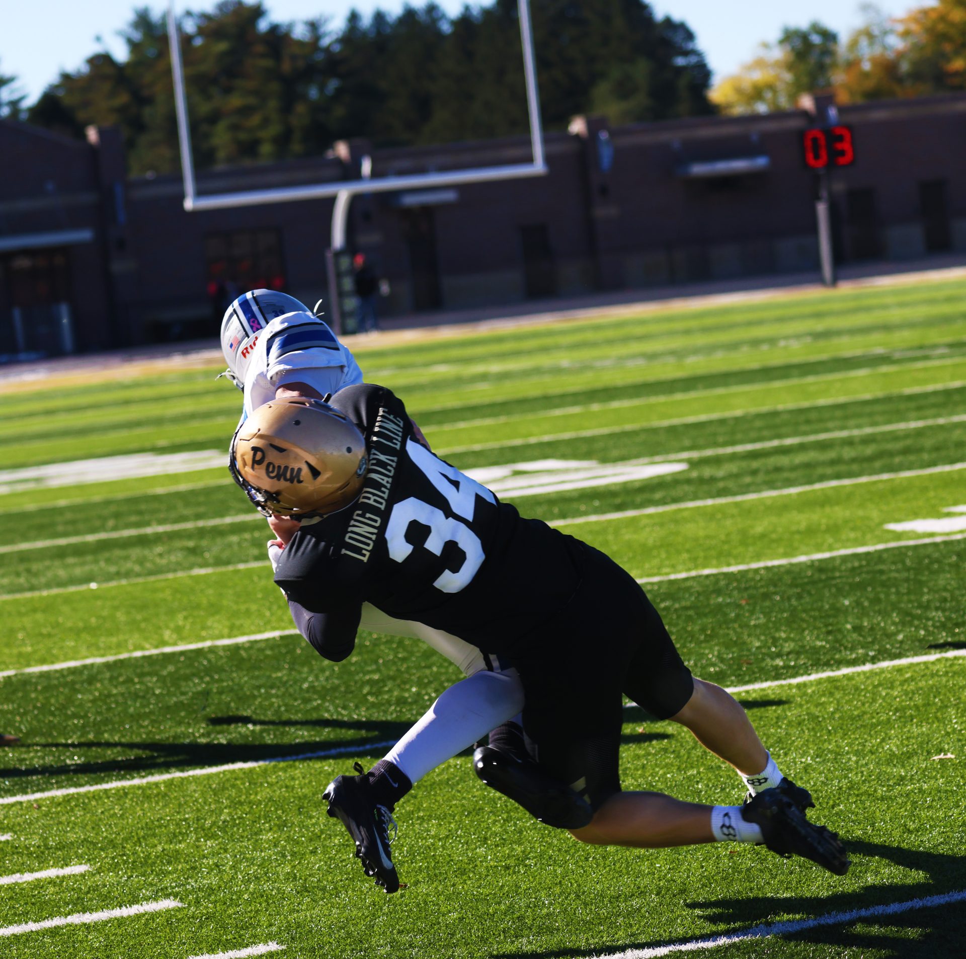 Football player in black uniform with number 34, in mid-air, reaching for a ball, with a white
