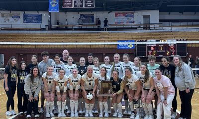 A group of female volleyball players posing for a team photo on a court.