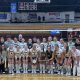 A group of female volleyball players posing for a team photo on a court.